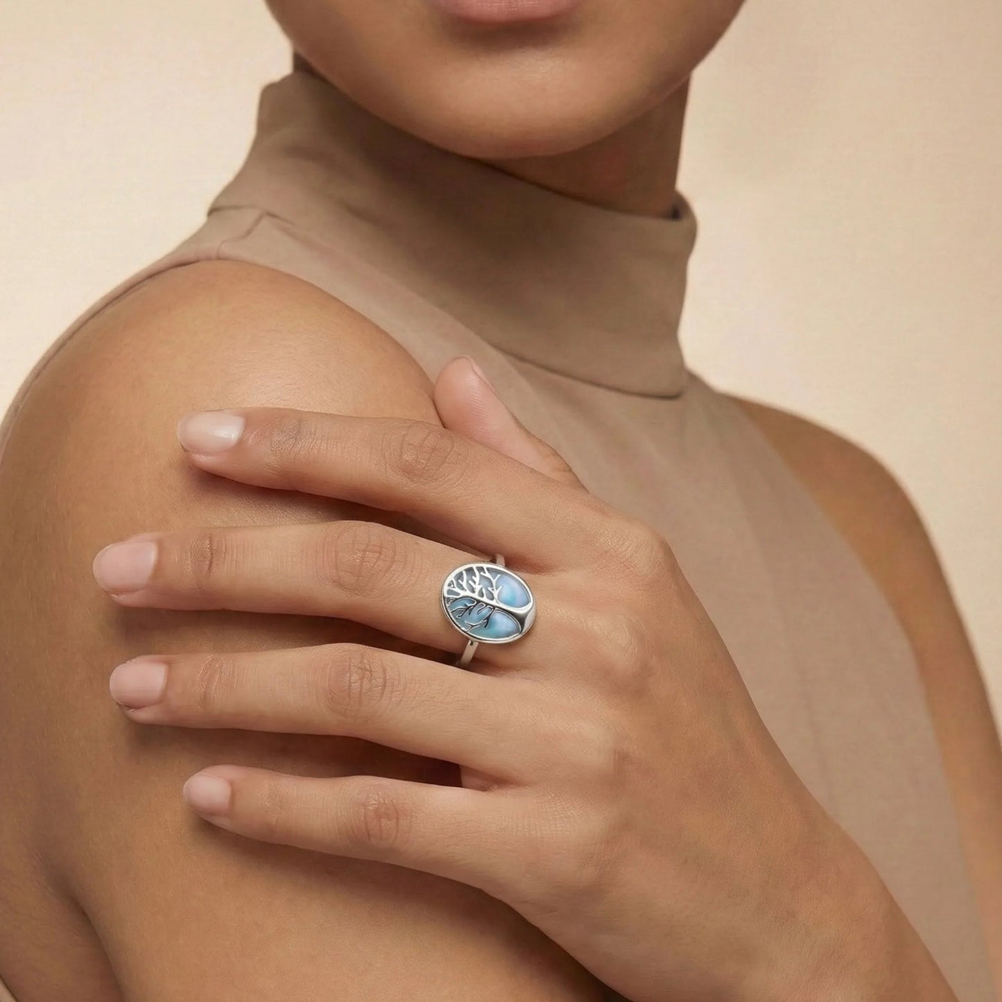 Woman wearing a ring with a blue gemstone on a beige background